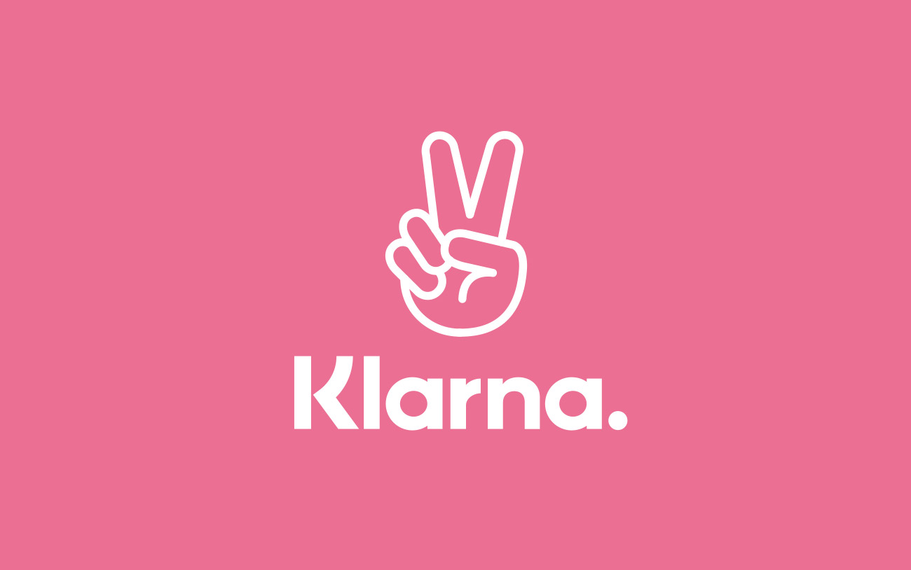Klarna-Logo in Weiß auf rosa Hintergrund mit Peace-Zeichen.